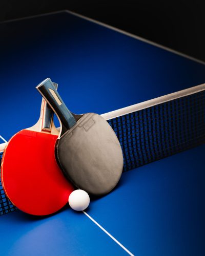 Two table tennis rackets and balls on a blue table with net.
